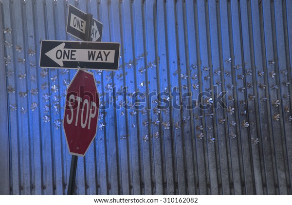 One Way\
Signs and Stop Sign in Front of Metal\
Wall