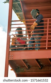 One welder observing another welder using welding torch on metal stairwell 