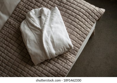 One White Bath Robe Laying On Bed Blanket Folded. Cotton Hotel SPA Clothing. Top View Clean Bathrobe Flat Lay.