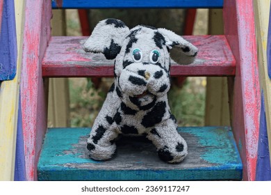 one white with black spots small soft beautiful gift for children to play funny toy old factory dog sitting on a green wooden step of a children's staircase during the day outdoors