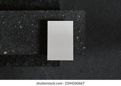 One white business card laying flat on a dark grey concrete surface, Modern clean minimalism mockup template for luxury stationery.