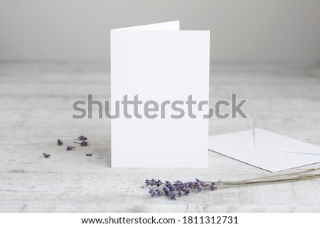 One white greeting card mockup, standing upright on a white wooden desk. Blank, closed card template with envelope. 