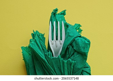 One White Plastic Fork Wrapped In A Green Paper Napkin On A Yellow Background