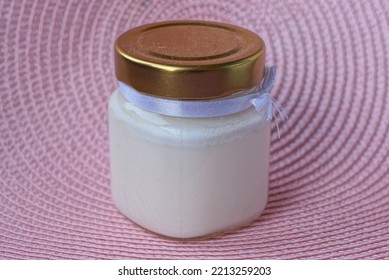 One White Scented Candle In A Glass Jar Closed With A Brown Lid Stands On A Pink Table