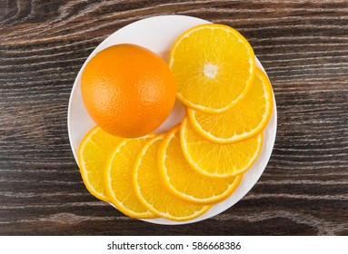 One Whole Orange And Slices Of Oranges In White Dish On Dark Wooden Table. Top View