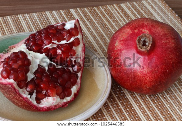 One whole\
ripe pomegranate fruit lies next to the slices of pomegranate.\
Bright ripe red pomegranate\
seeds.