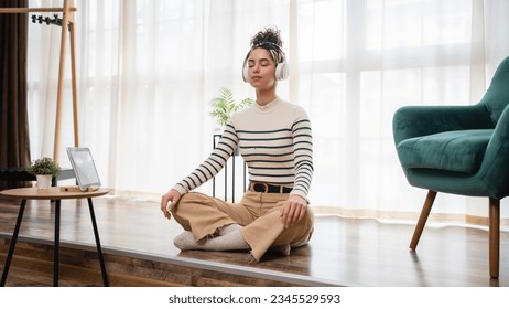 one woman adult caucasian female millennial using headphones for online guided meditation practicing mindfulness yoga with eyes closed on the floor at home real people self care concept copy space