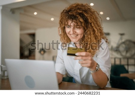 One woman adult caucasian female with curly hair happy smile use credit card shopping online on laptop computer at cafe real people e-banking internet sale purchase copy space positive emotion