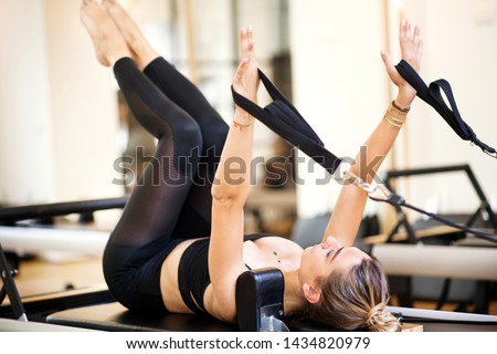 One woman in black outfit lying on her back doing supine arm work on pilates bed