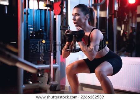 One woman doing goblet squat exercise in a gym with a dumbbell