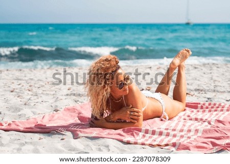 One woman laying at the beach having relaxation and sunbathing in summer holiday vacation. Blue ocean sea in background. Outdoor leisure activity. Skin care sun. Blonde long curly hair pretty female