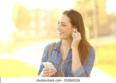 One woman listening music with earphones in the street at sunset with a warm light in the background - Powered by Shutterstock