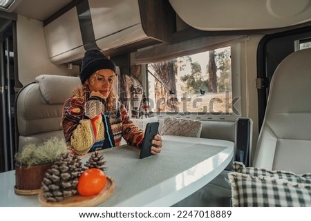 One woman living inside a modern camper van motorhome sitting at the table and using mobile phone to stay connected. Roaming connection technology for traveler female people in van life lifestyle