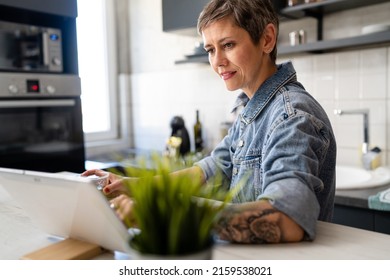 One Woman Mature Caucasian Female Having A Cup Of Coffee In The Kitchen While Using Digital Tablet Daily Morning Routine Checking Mail Or Daily Tasks While Preparing For Work Real People Copy Space