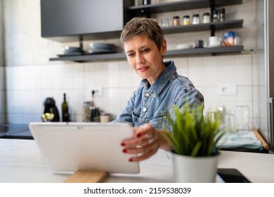 One Woman Mature Caucasian Female Having A Cup Of Coffee In The Kitchen While Using Digital Tablet Daily Morning Routine Checking Mail Or Daily Tasks While Preparing For Work Real People Copy Space