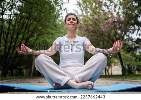 one woman mature caucasian senior female sit outdoor on yoga mat meditate front view real people meditation self-care manifestation practice mental emotional balance concept