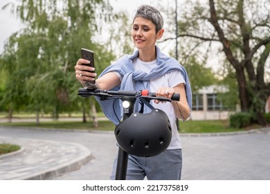 One Woman Mature Senior Caucasian Female Standing Outdoor Use Mobile Phone For Selfie Photos Or Video Call By Electric Kick Scooter In Day Confident Modern Alternative Mode Of Transport Copy Space