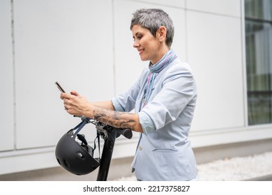 One Woman Mature Senior Caucasian Female Standing Outdoor Use Mobile Phone For Selfie Photos Or Video Call By Electric Kick Scooter In Day Confident Modern Alternative Mode Of Transport Copy Space Sms