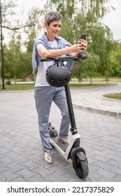 One Woman Mature Senior Caucasian Female Standing Outdoor Use Mobile Phone For Selfie Photos Or Video Call By Electric Kick Scooter In Day Confident Modern Alternative Mode Of Transport Copy Space