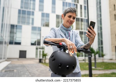 One Woman Mature Senior Caucasian Female Standing Outdoor Use Mobile Phone For Selfie Photos Or Video Call By Electric Kick Scooter In Day Confident Modern Alternative Mode Of Transport Copy Space Sms