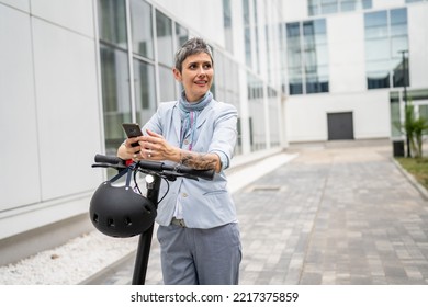 One Woman Mature Senior Caucasian Female Standing Outdoor Use Mobile Phone For Selfie Photos Or Video Call By Electric Kick Scooter In Day Confident Modern Alternative Mode Of Transport Copy Space Sms