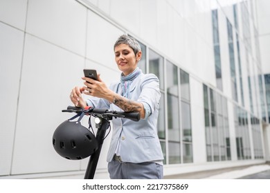 One Woman Mature Senior Caucasian Female Standing Outdoor Use Mobile Phone For Selfie Photos Or Video Call By Electric Kick Scooter In Day Confident Modern Alternative Mode Of Transport Copy Space