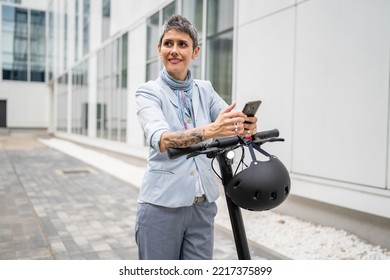 One Woman Mature Senior Caucasian Female Standing Outdoor Use Mobile Phone For Selfie Photos Or Video Call By Electric Kick Scooter In Day Confident Modern Alternative Mode Of Transport Copy Space Sms