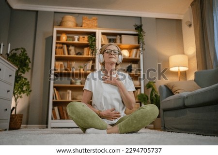 one woman mature senior caucasian female using headphones for online guided meditation practicing mindfulness yoga manifestation with eyes closed at home real people self care concept copy space