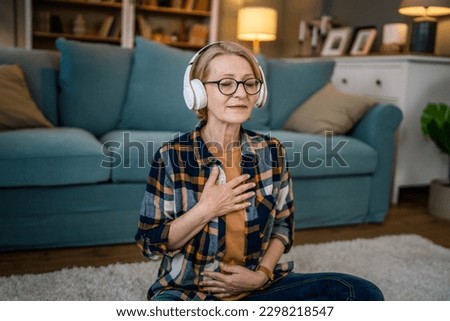 one woman mature senior caucasian female using headphones for online guided meditation practicing mindfulness yoga manifestation with eyes closed at home real people self care concept copy space