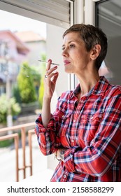 One Woman Mature Or Senior Female Smoking Cigarette By The Window At Home In Bright Day Real People Copy Space Daily Routine Unhealthy Habit Nicotine Addiction Serious Looking Out Waiting Worried