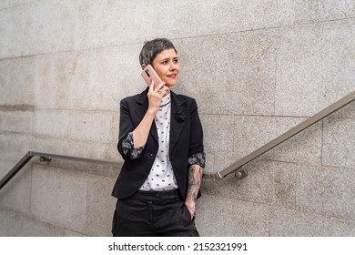 One Woman Modern Mature Caucasian Female Businesswoman With Short Hair Using Mobile Phone Making A Call Talk While Walking On The Stairs By Building In Day Against Concrete Or Stone Wall Copy Space