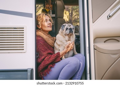 One woman sitting on the camper van door with old nice pug dog looking outside and enjoying relax and freedom. Female people living on a rv motorhome with animals and travel the world. Best friend