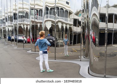 One Woman Standing On A Street In Front Of A Len Lye (crooked) Mirror And Looking To Her Distorted Reflection