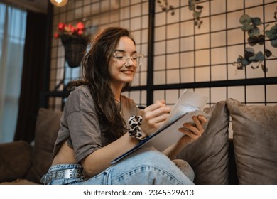 One woman young adult caucasian female student sitting on the sofa bed at home reading papers preparing exam study alone real people education concept copy space - Powered by Shutterstock