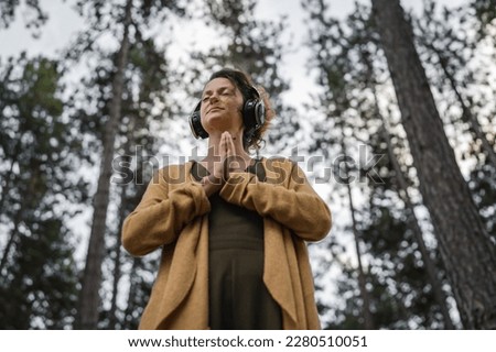 One woman young adult caucasian female stand alone in the park or forest in nature with headphones preparing for guided meditation self-care manifestation practice mental emotional balance concept