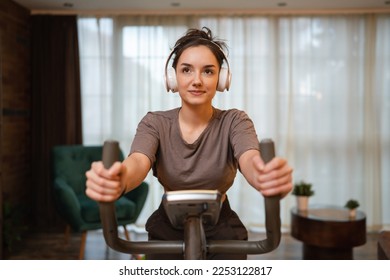 One woman young caucasian female training at home with headphones on Indoor Cycling stationary Exercise Bike real people copy space health and fitness workout concept front view - Powered by Shutterstock