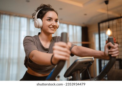 One woman young caucasian female training at home with headphones on Indoor Cycling stationary Exercise Bike real people copy space health and fitness workout concept happy smile - Powered by Shutterstock