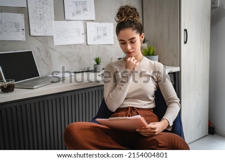 one woman young caucasian female sitting by the desk at work in the office study documents relaxing while hold clip chart with papers real people copy space female engineer or student planning project