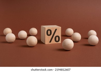 One Wooden Cube With Percent Symbol Printed And Many Wooden Balls, Viewed In Close-up With Shadow On Brown Background