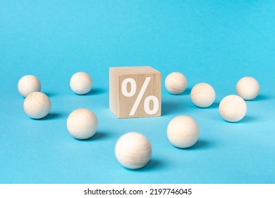 One Wooden Cube With Percent Symbol Printed And Many Wooden Balls, Viewed In Close-up With Shadow On Blue Background