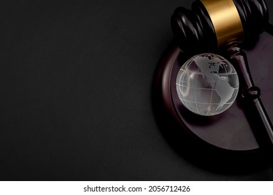 One World Government, Worldwide Global Legal System And International Law Concept With Wooden Judge Gavel And Glass Atlas Or Globe Isolated On Black Background With Copy Space