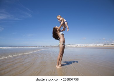 one year baby swimsuit fly in bikini woman mother arms at beach next to Conil Cadiz Spain