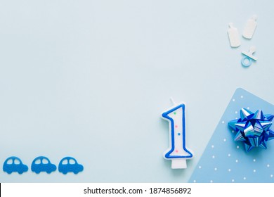 One year concept. Candle in shape of number one lies on blue background with children's accessories. Boy birthday concept. Greeting card. Copy space.