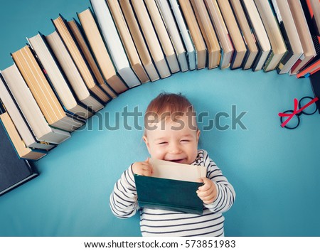 One year old baby among books with spectackles.Happy little child reading