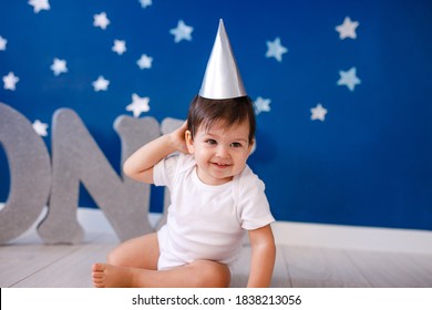 One year old baby boy celebrates birthday near silver letters ONE on blue background with stars.