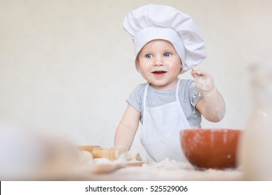 One year old baby boy in a suit of the cook surprised and smiling in the kitchen. Small kid as a little cook or scullion make pizza in chef suit. Cooking child lifestyle concept. Toddler playing