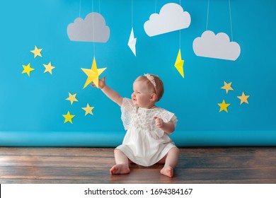 Ein Jahr altes Baby feiert Geburtstag. Fotozone. Kleid in weißer Farbe. Sie berührt einen papiergelben Stern. 