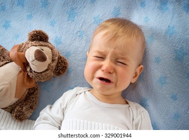 One year old baby crying in bed with a teddy bear