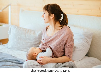 One year old baby eating mother's milk. Mother breastfeeding infant baby boy, siting on bed in cozy bedroom at home interior. Concept of lactation infant.