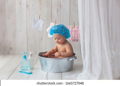 Ein Jahr altes Mädchen badet. In blauer Schwimmkappe. Bad. Das Mädchen badet in einem Waschbecken. Kleidung wird auf einem Kleiderbügel getrocknet. Bademäntel.
